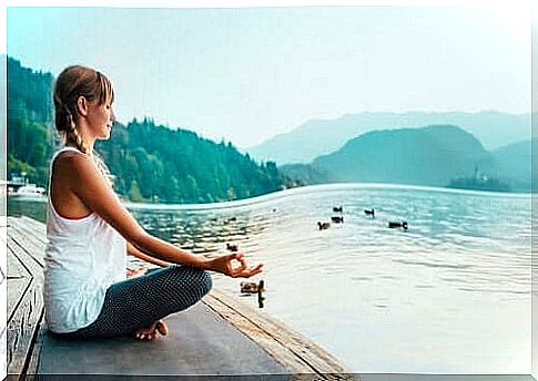 Woman meditating by lake.